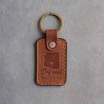 Sandy tan leather keychain debossed with a solid Arizona silhouette and a heart at Phoenix above Dry heat and ARIZONA, on gray concrete