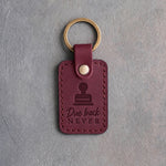 Sangria wine red leather keychain debossed with a library date stamp above Due back and NEVER, on gray concrete