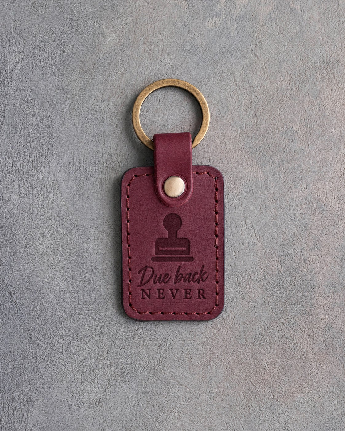 Sangria wine red leather keychain debossed with a library date stamp above Due back and NEVER, on gray concrete