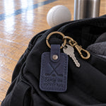Navy Early Ice Hockey Dad keychain on truck keys beside a hockey bag in a dark rink parking lot