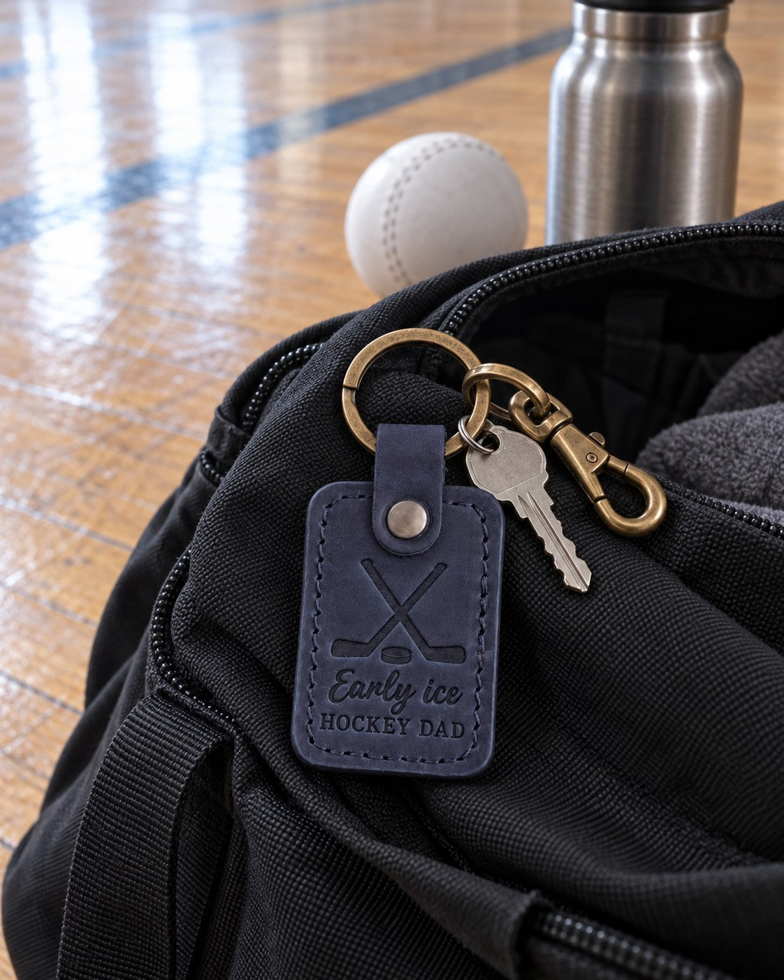 Navy Early Ice Hockey Dad keychain on truck keys beside a hockey bag in a dark rink parking lot