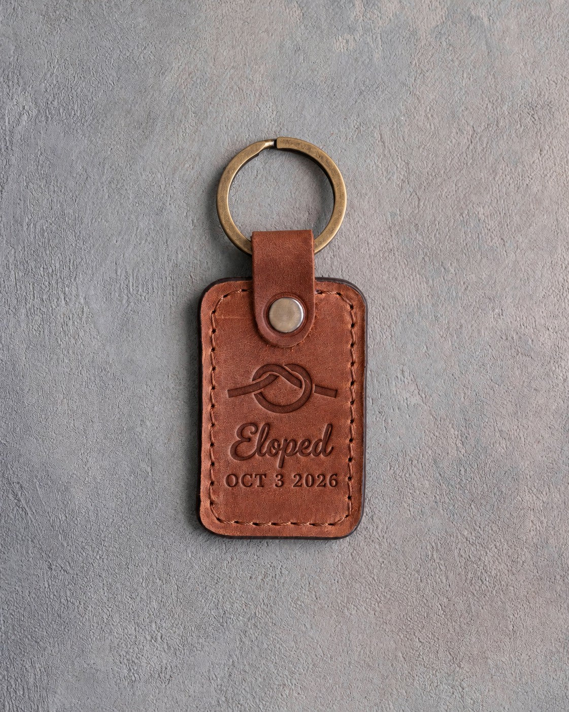 Arizona tan leather keychain debossed with an overhand rope knot above Eloped and OCT 3 2026, on gray concrete