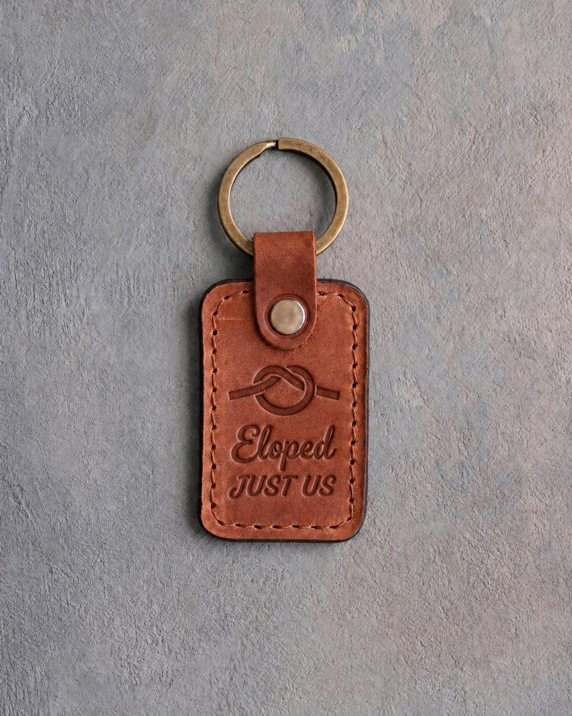 Arizona tan leather keychain debossed with an overhand rope knot above Eloped and JUST US, on gray concrete