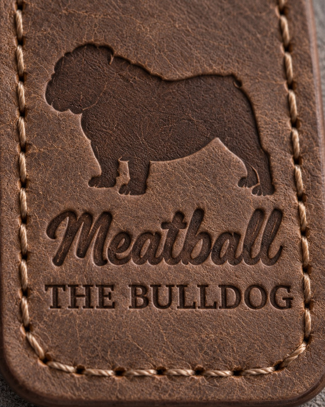 Close-up of Meatball and THE BULLDOG pressed into brown full-grain leather under a stocky bulldog silhouette