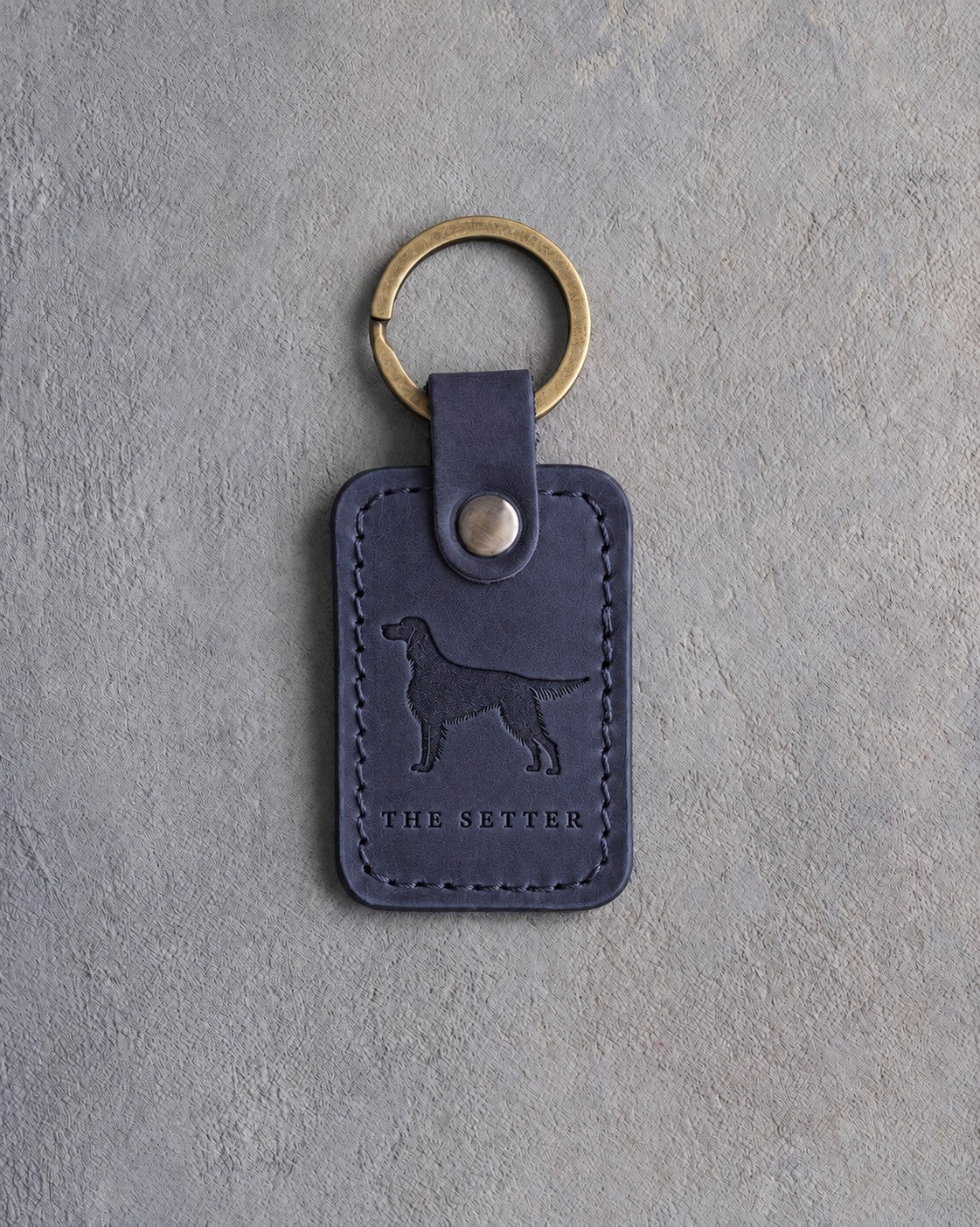 Blueberry navy leather keychain debossed with an English Setter silhouette above THE SETTER, on gray concrete