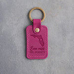 Fuchsia pink leather keychain debossed with a Florida silhouette and a heart at Orlando above Even miss THE HUMIDITY, on gray concrete