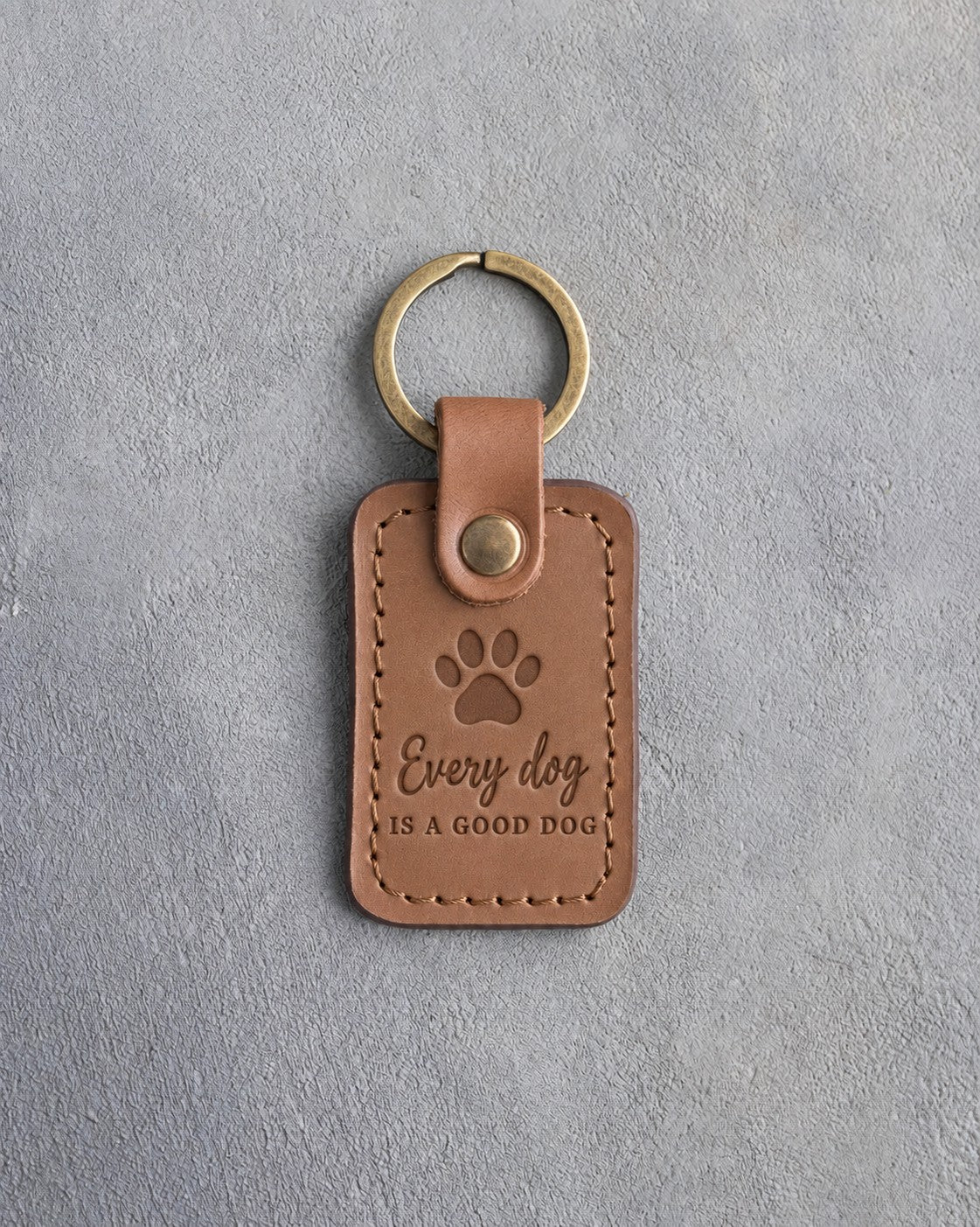 Caramel leather keychain debossed with a paw print and the words Every dog IS A GOOD DOG, on gray concrete