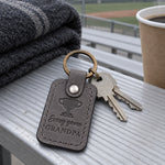 Gray Every Game Grandpa keychain on an aluminum bleacher plank with a coffee cup and empty rows below