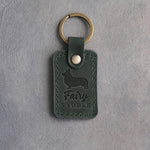 Forest green leather keychain debossed with a Pembroke corgi silhouette and the words Fairy SADDLE, on gray concrete