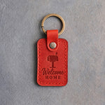 Poppy red leather keychain debossed with a roadside mailbox above Welcome and HOME, on gray concrete