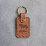 Caramel leather keychain debossed with a steer silhouette above the name Walker and CATTLE, on gray plaster