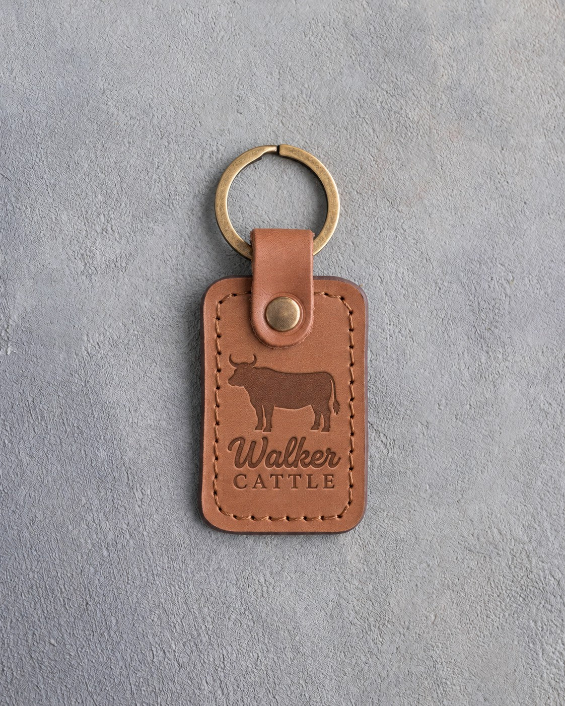 Caramel leather keychain debossed with a steer silhouette above the name Walker and CATTLE, on gray plaster