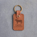 Caramel leather keychain debossed with a steer silhouette above Cattle and COUNTRY, on gray concrete