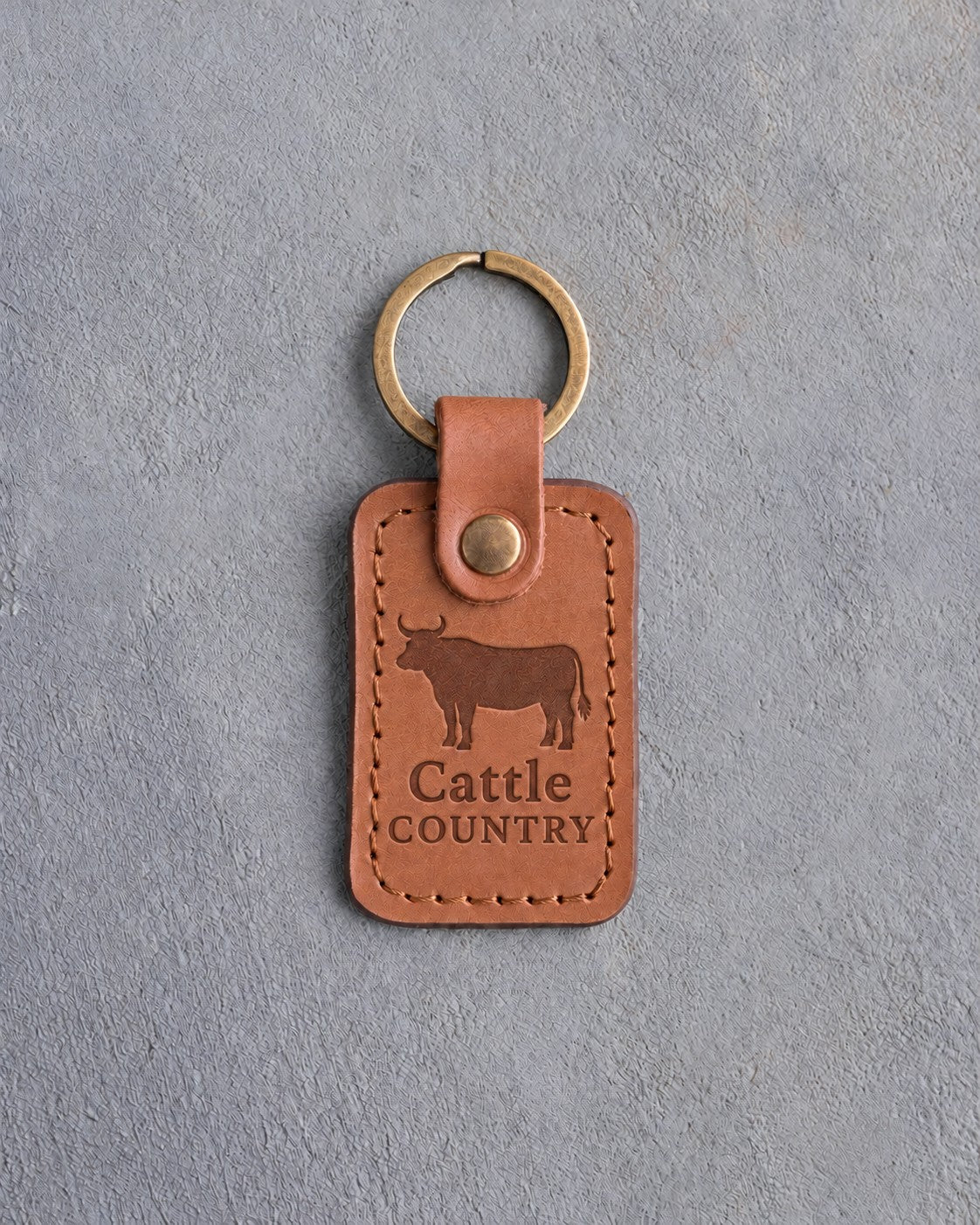 Caramel leather keychain debossed with a steer silhouette above Cattle and COUNTRY, on gray concrete