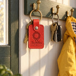 Red The Millers DECEMBER 2026 keychain hanging from a Christmas tree beside a stack of holiday cards
