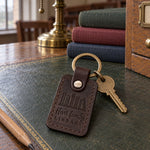 Dark brown Hart family LIBRARY keychain on an oak reading table beside cloth-bound books and an unlit banker's lamp