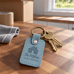 Turquoise The Millers LAKE HOUSE keychain hanging from a hook by a cabin door above a lake