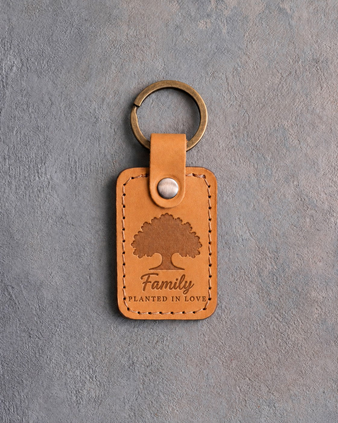 Indian Summer golden tan leather keychain debossed with a solid oak tree above Family and PLANTED IN LOVE, on gray concrete