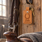 Dale FARRIER keychain in Indian Summer leather hanging from a forged iron bridle hook on rough pine boards in a tack room