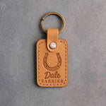 Indian Summer tan leather keychain debossed with a heels-up horseshoe above the name Dale and FARRIER, on gray plaster