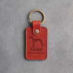 Poppy red leather keychain debossed with a greyhound and the words Fastest COUCH POTATO, on gray concrete
