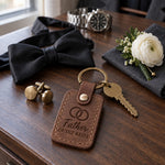 Father OF THE BRIDE keychain in reddish brown leather on a walnut dresser beside cufflinks and a wristwatch