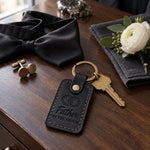 Father OF THE GROOM keychain in black leather on a walnut hotel dresser beside cufflinks and an untied black bow tie