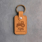 Golden tan leather keychain debossed with a cab tractor above the words Fifth and GENERATION, on gray plaster