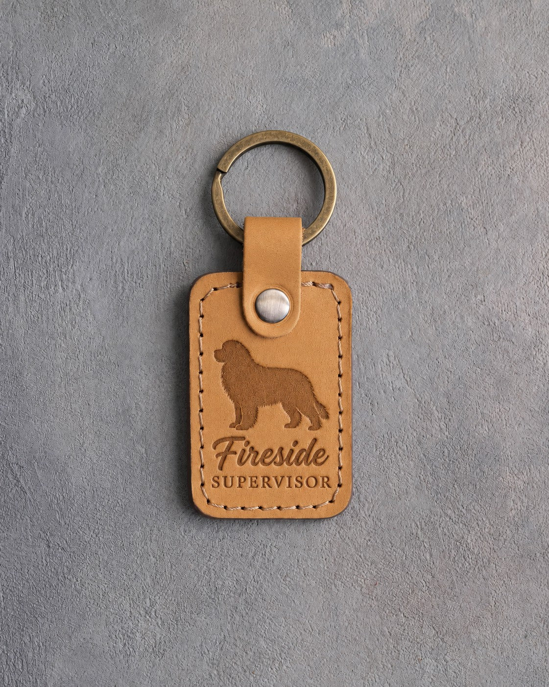 Indian Summer tan leather keychain debossed with a Newfoundland silhouette and the words Fireside SUPERVISOR, on gray concrete