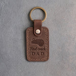 Sicilian brown leather keychain debossed with a coach's whistle and the words First coach DAD, on gray plaster