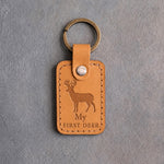 Golden tan leather keychain debossed with a whitetail buck above My and FIRST DEER, on gray concrete