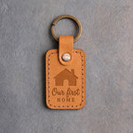 Indian Summer golden tan leather keychain debossed with a gabled house above Our first and HOME, on gray concrete