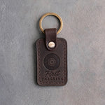 Dark espresso leather keychain debossed with a vinyl record above the words First PRESSING, on gray plaster