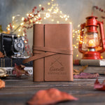 Caramel leather wrap journal with its strap tied, the lower cover debossed with crossed fishing rods above Garrett and FISHING LOG
