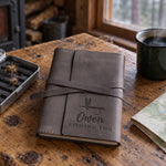Country gray Owen FISHING LOG journal in full-grain leather on a knotty pine cabin table beside an open fly box and a green enamel coffee mug