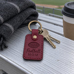 Wine red Football Mom keychain on car keys resting on a stadium blanket under evening lights