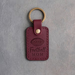 Sangria wine red leather keychain debossed with a football and the words Football MOM, on gray plaster