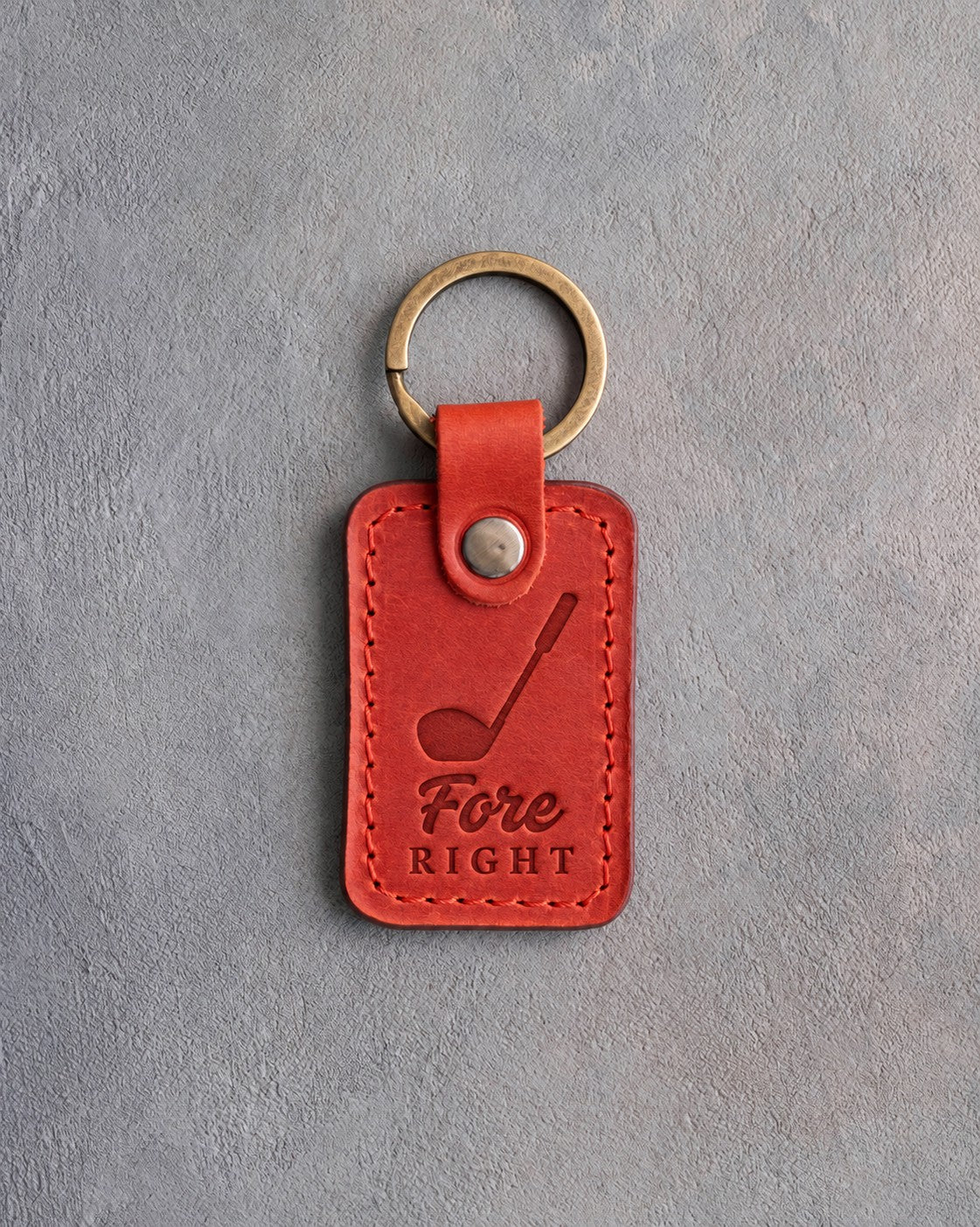 Poppy red leather keychain debossed with a golf driver above the words Fore RIGHT, on gray plaster