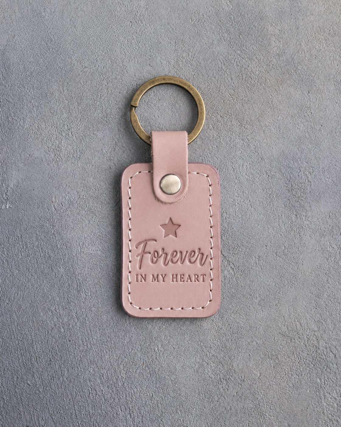 Blush pink leather keychain debossed with one small star above the words Forever IN MY HEART, on gray concrete
