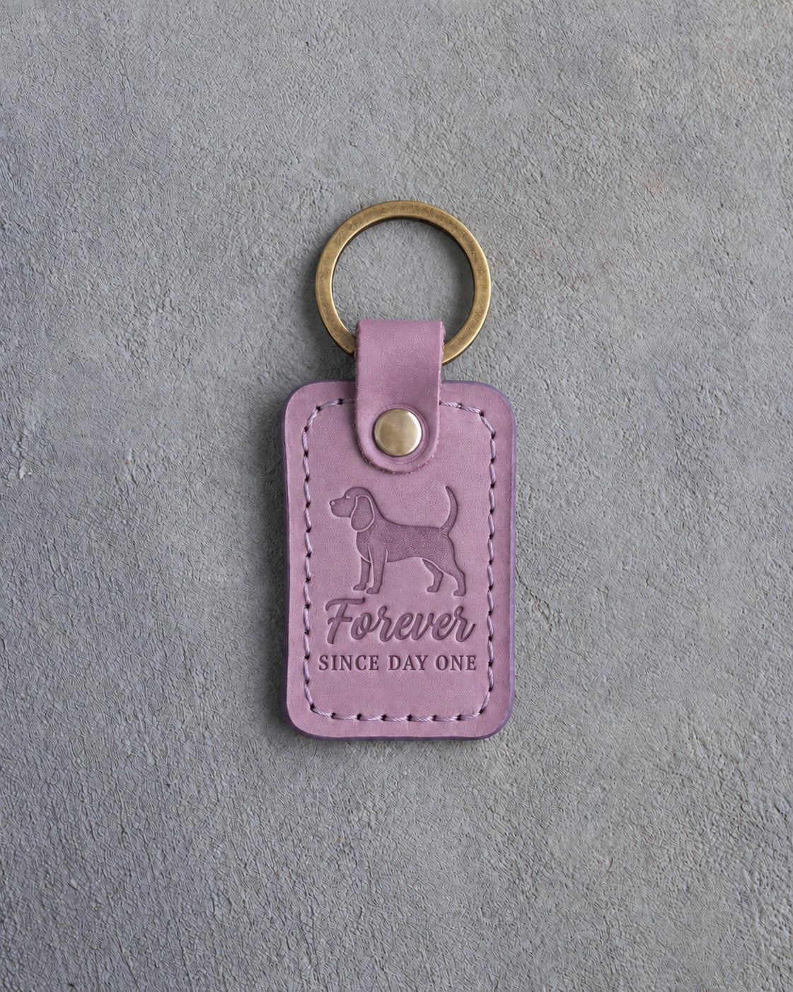 Lilac leather keychain debossed with a beagle and the words Forever SINCE DAY ONE, on gray concrete