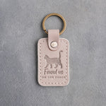 Gray sand leather keychain debossed with a cat walking with its tail up above the words Found us ON THE PORCH
