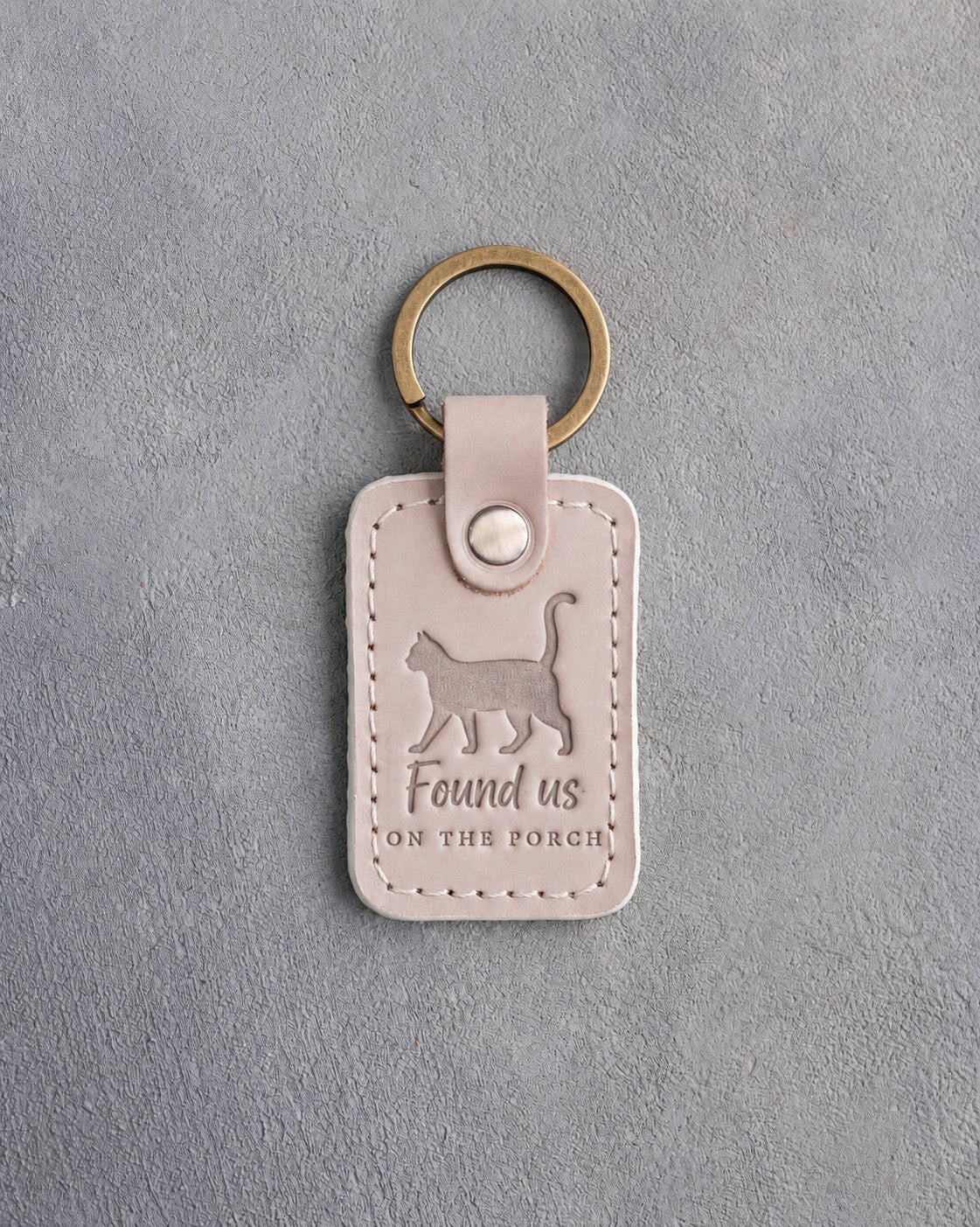 Gray sand leather keychain debossed with a cat walking with its tail up above the words Found us ON THE PORCH