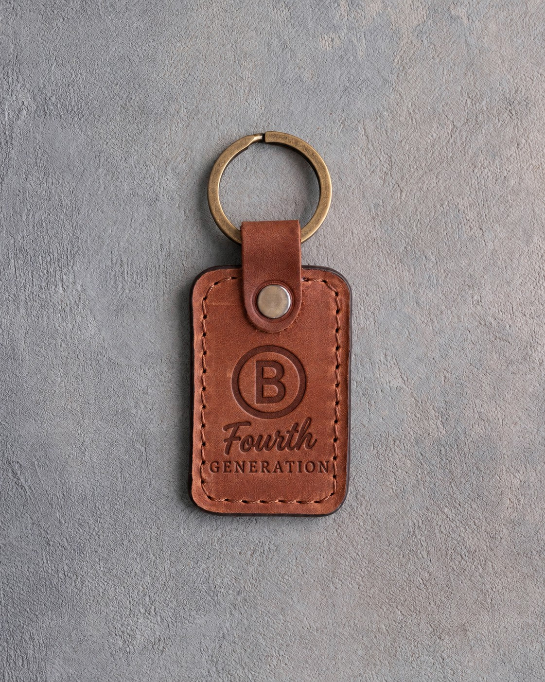 Arizona leather keychain debossed with a Circle B ranch brand above Fourth and GENERATION, on gray plaster
