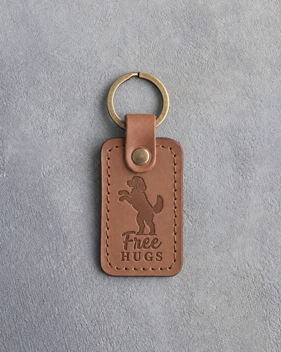 Caramel leather keychain debossed with a goldendoodle standing on its hind legs and the words Free HUGS, on gray concrete