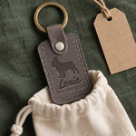 Louie the Frenchie keychain in gray leather tucked into a cotton gift pouch on green linen beside a kraft tag