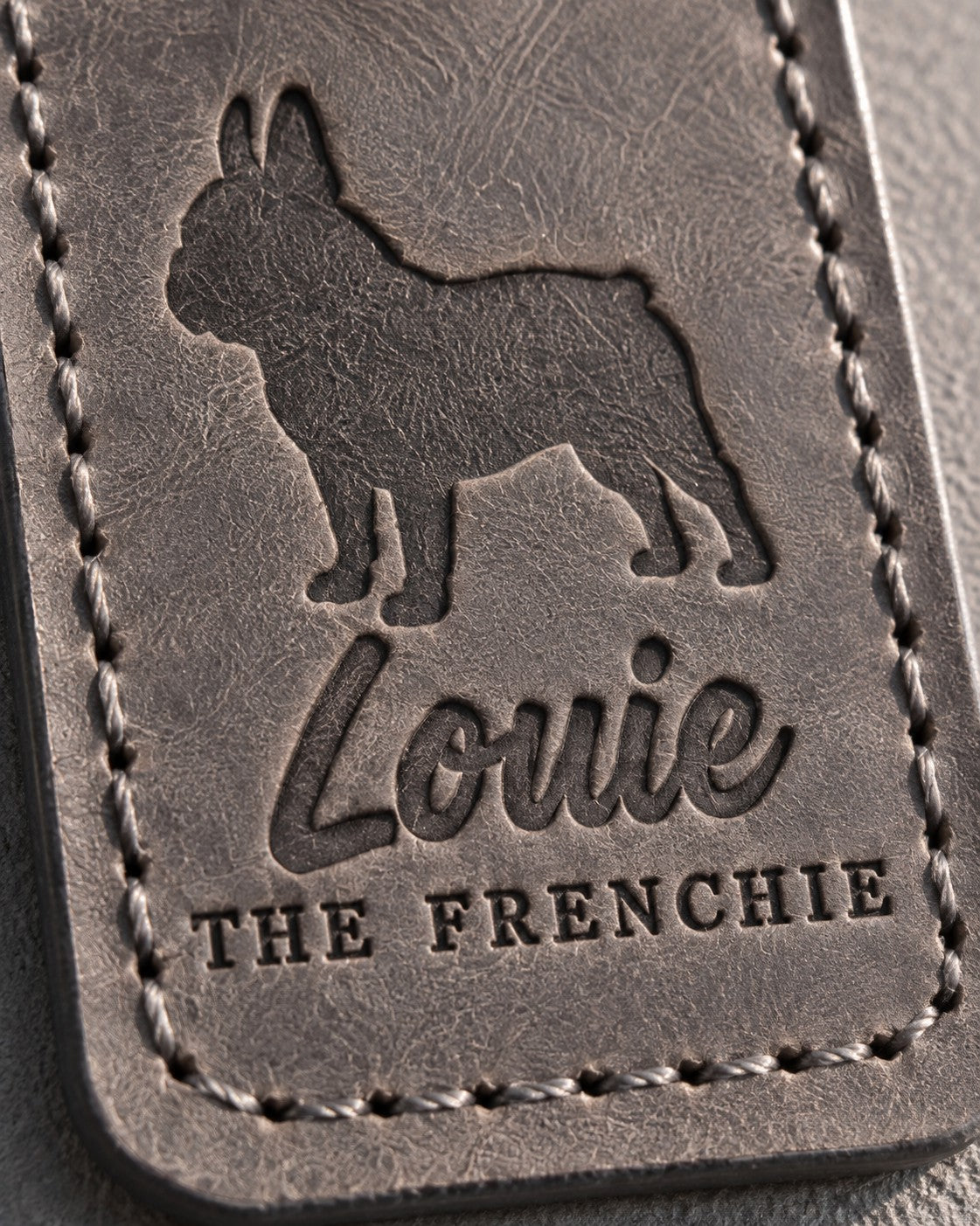 Close-up of the name Louie and THE FRENCHIE debossed in gray full-grain leather under a bat-eared French bulldog
