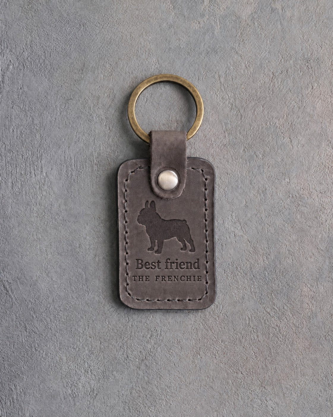 Country gray leather keychain with a debossed French bulldog above Best friend and THE FRENCHIE, on gray concrete