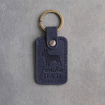 Blueberry navy leather keychain with a debossed French bulldog and Frenchie DAD lettering, on gray concrete