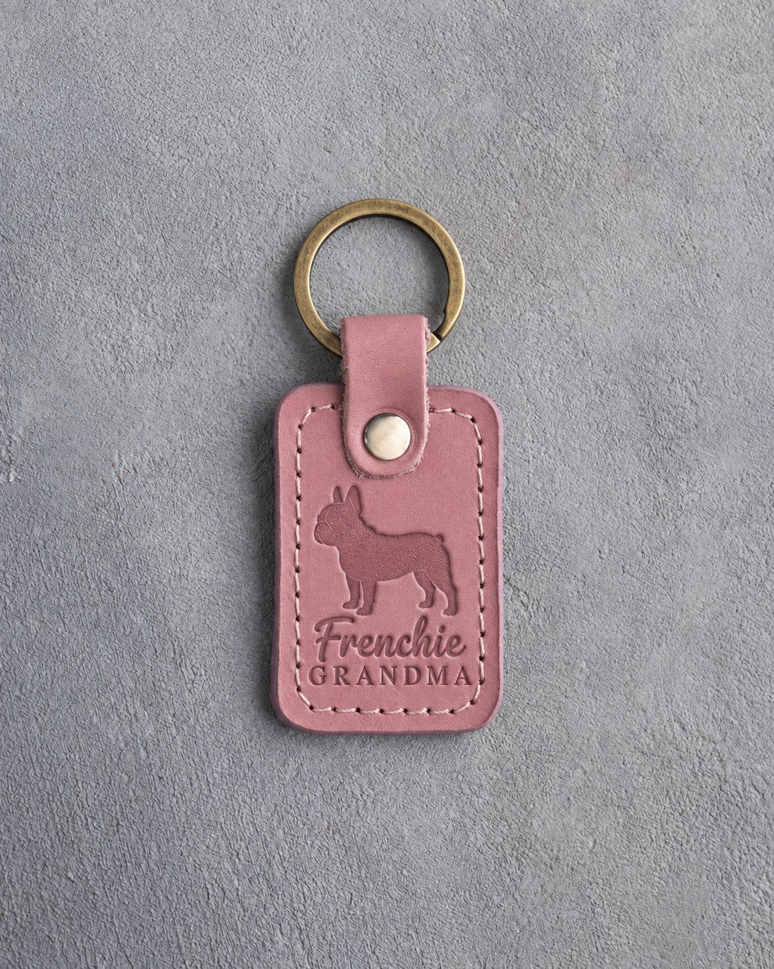 Parisian Blossom pink leather keychain debossed with a French bulldog silhouette and the words Frenchie GRANDMA, on gray concrete