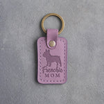 Lilac leather keychain debossed with a French bulldog silhouette and the words Frenchie MOM on gray concrete